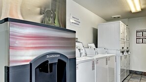 A laundromat with a Scotman self-service washing machine, multiple dryers, and a sign indicating the motel is not responsible for items left unattended. - Motel 6 Glenview, IL - Chicago North (Glenview)