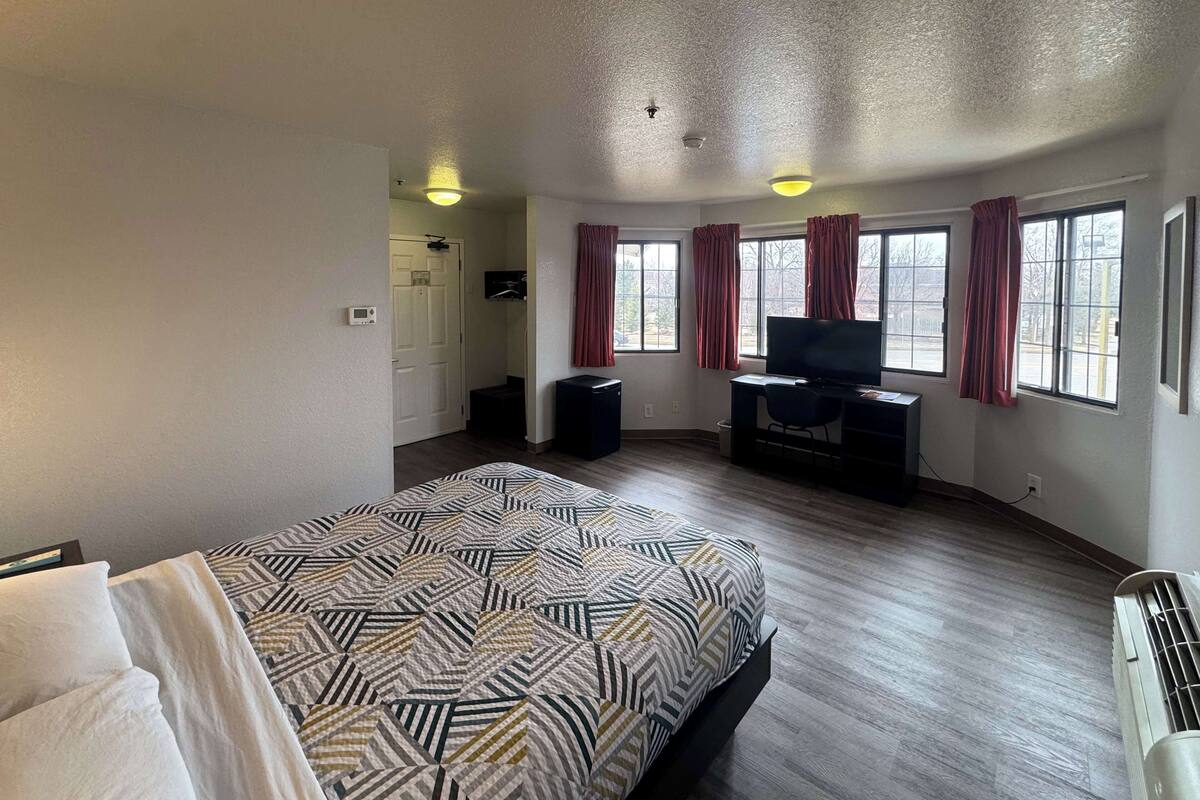 A spacious hotel room with a large bed, a desk with a computer, a television, and a window with curtains.