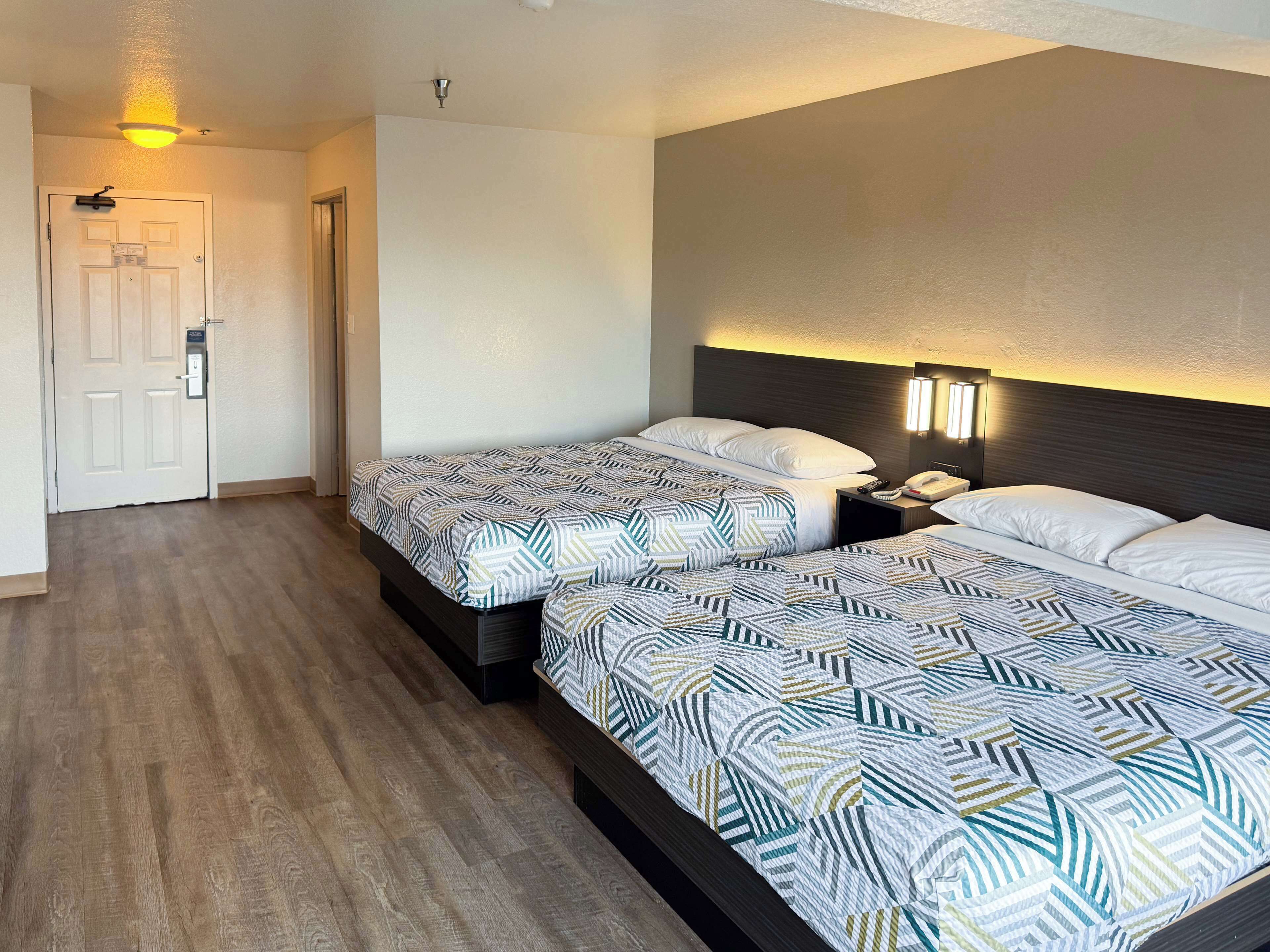 A hotel room with two beds, a nightstand, a phone, and a wall-mounted light fixture.