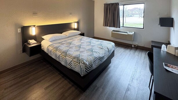 A modern hotel room with a large bed, bedside lamps, a desk, and a window with curtains. - Motel 6 Glenview, IL - Chicago North (Glenview)