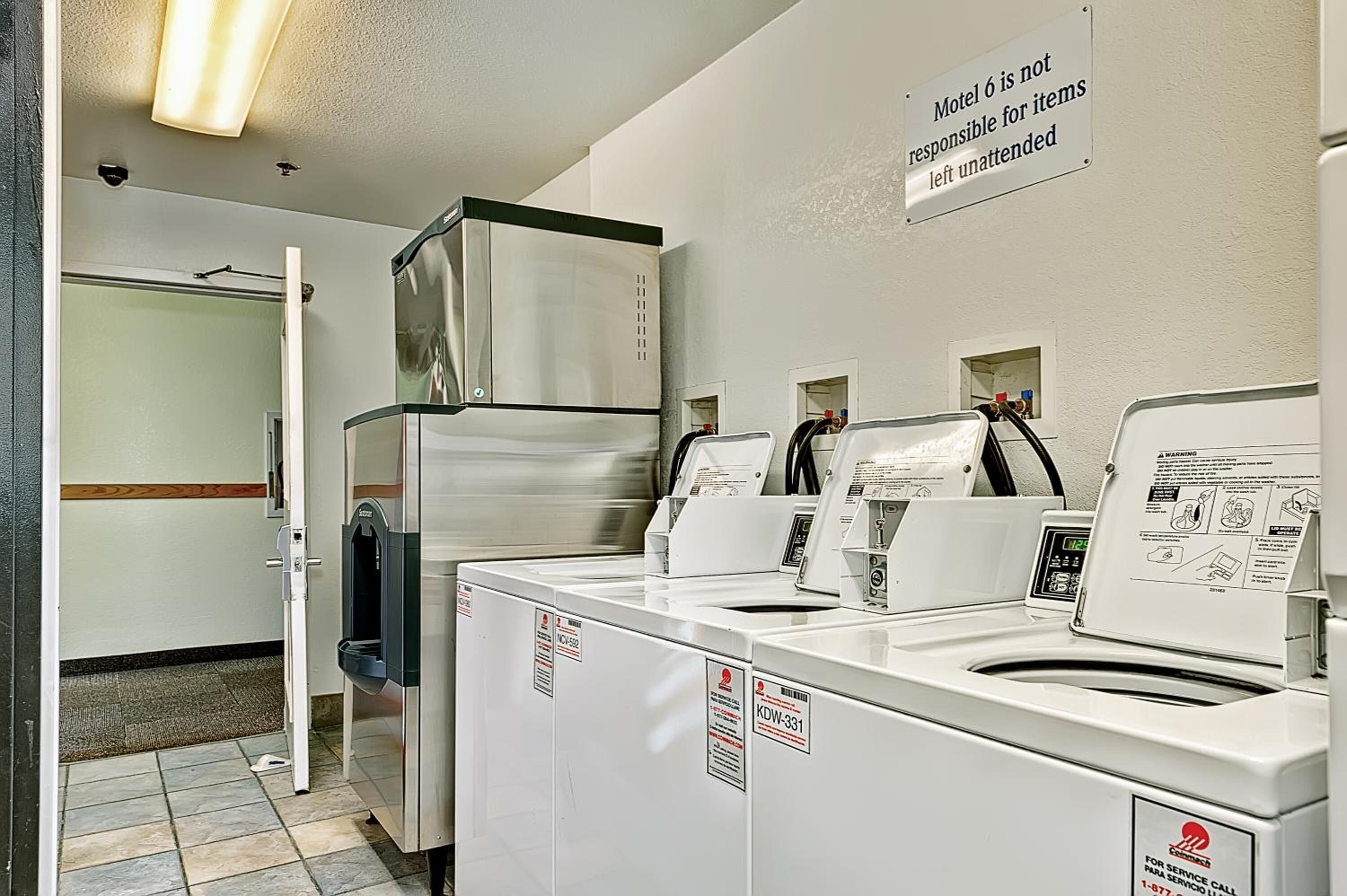 A laundry area with multiple washers and dryers, a sign indicating the motel is not responsible for unattended items, and a service call number on the machines.