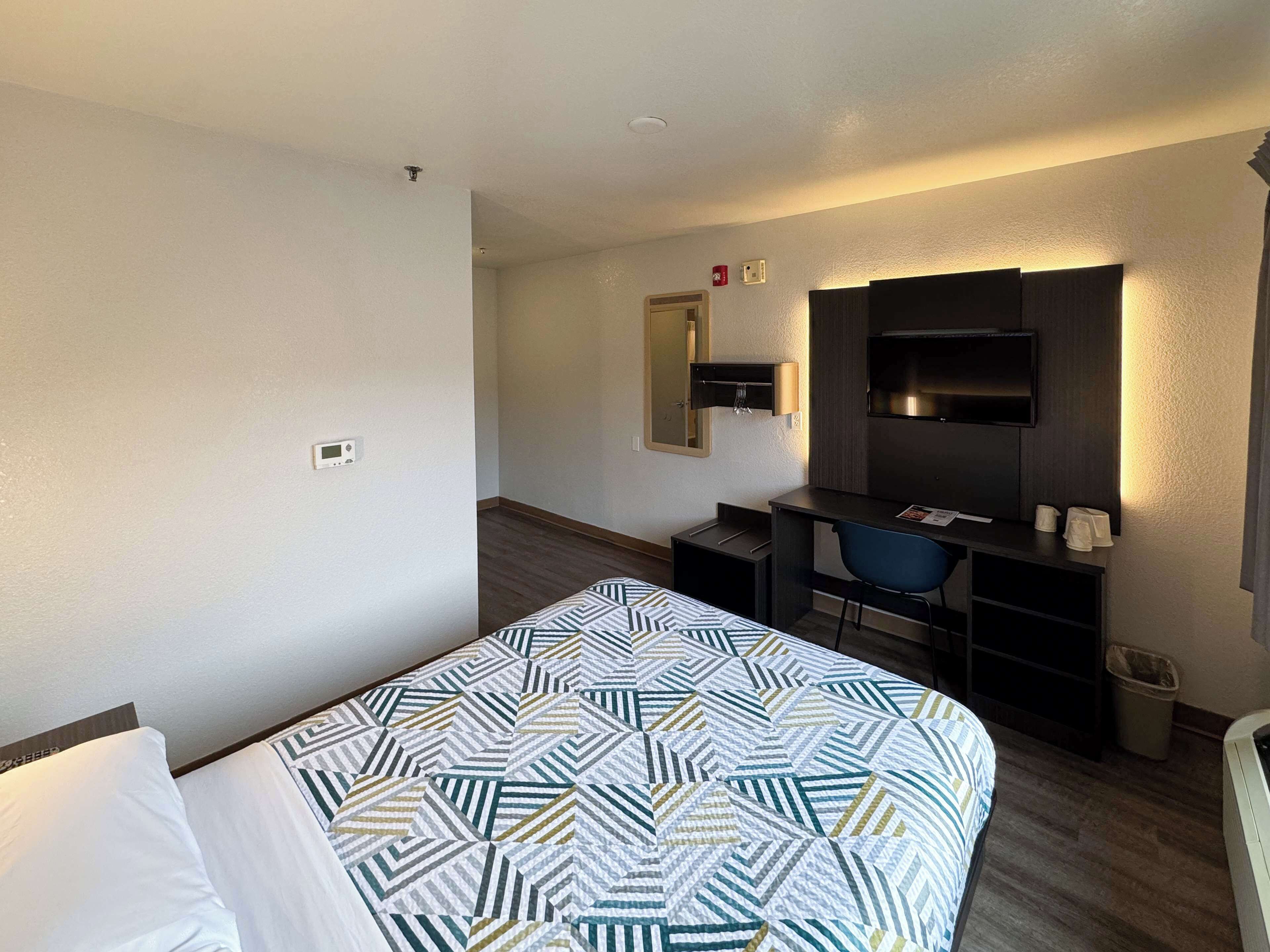 A hotel room with a bed, a desk, a chair, a TV, and a mirror.