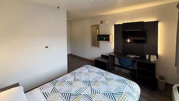 A hotel room with a bed, a desk, a chair, a TV, and a mirror.