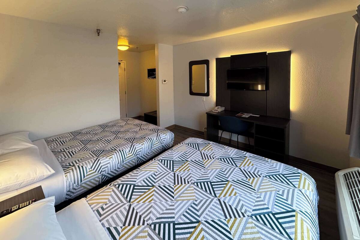 A hotel room with two single beds, a desk with a chair, a TV, and a mirror.