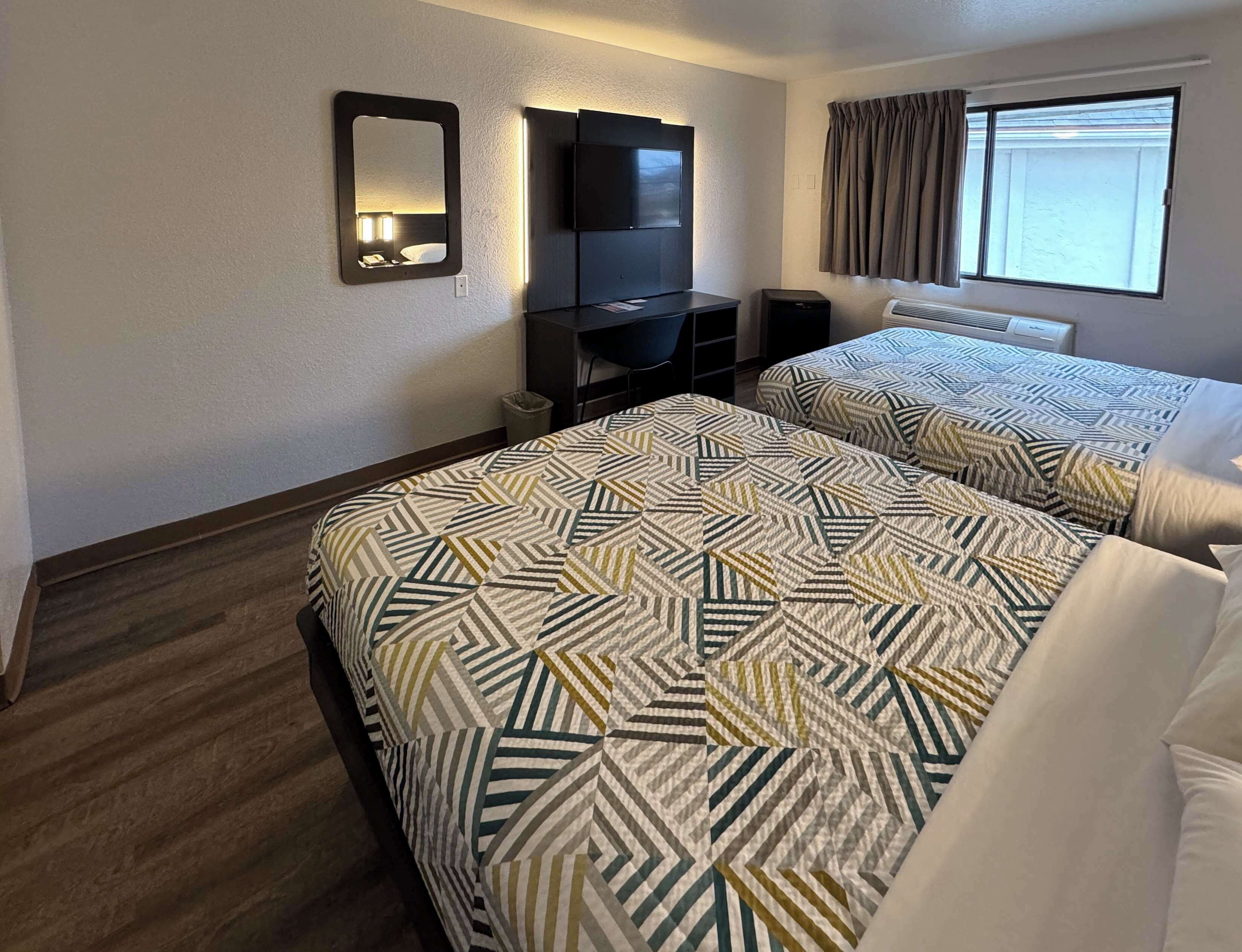 Una habitación de hotel con dos camas, televisión, escritorio y ventana con cortinas.