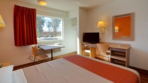A hotel room with a bed, a desk with a chair, a television, and a window with curtains.