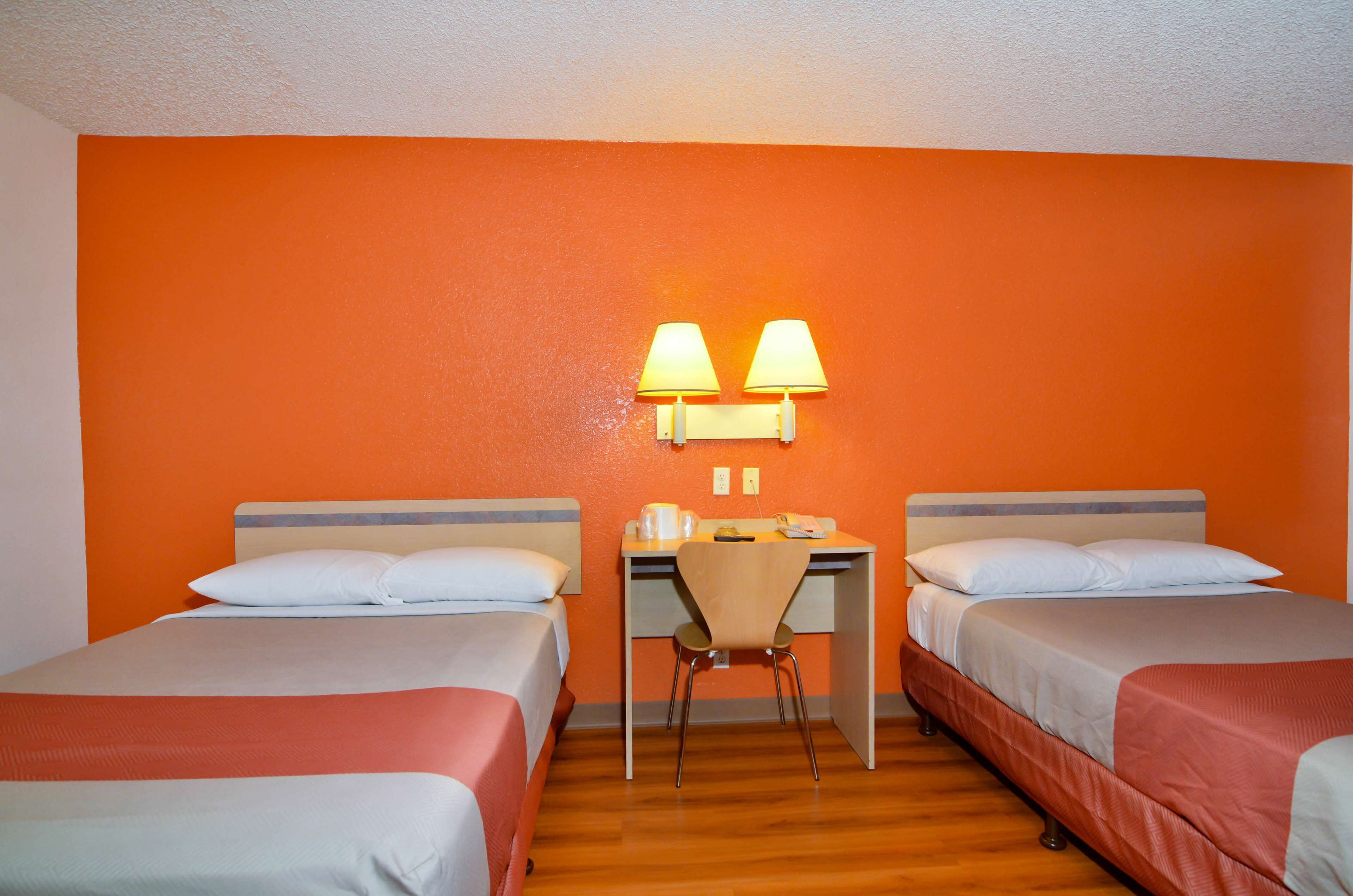 A hotel room with two beds, a desk, and two wall-mounted lamps.