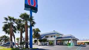 A motel with a prominent '6' sign, palm trees, and a parking lot with vehicles.