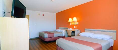 Quarto de hotel com duas camas, uma televisão, uma escrivaninha com candeeiro e chão de madeira.