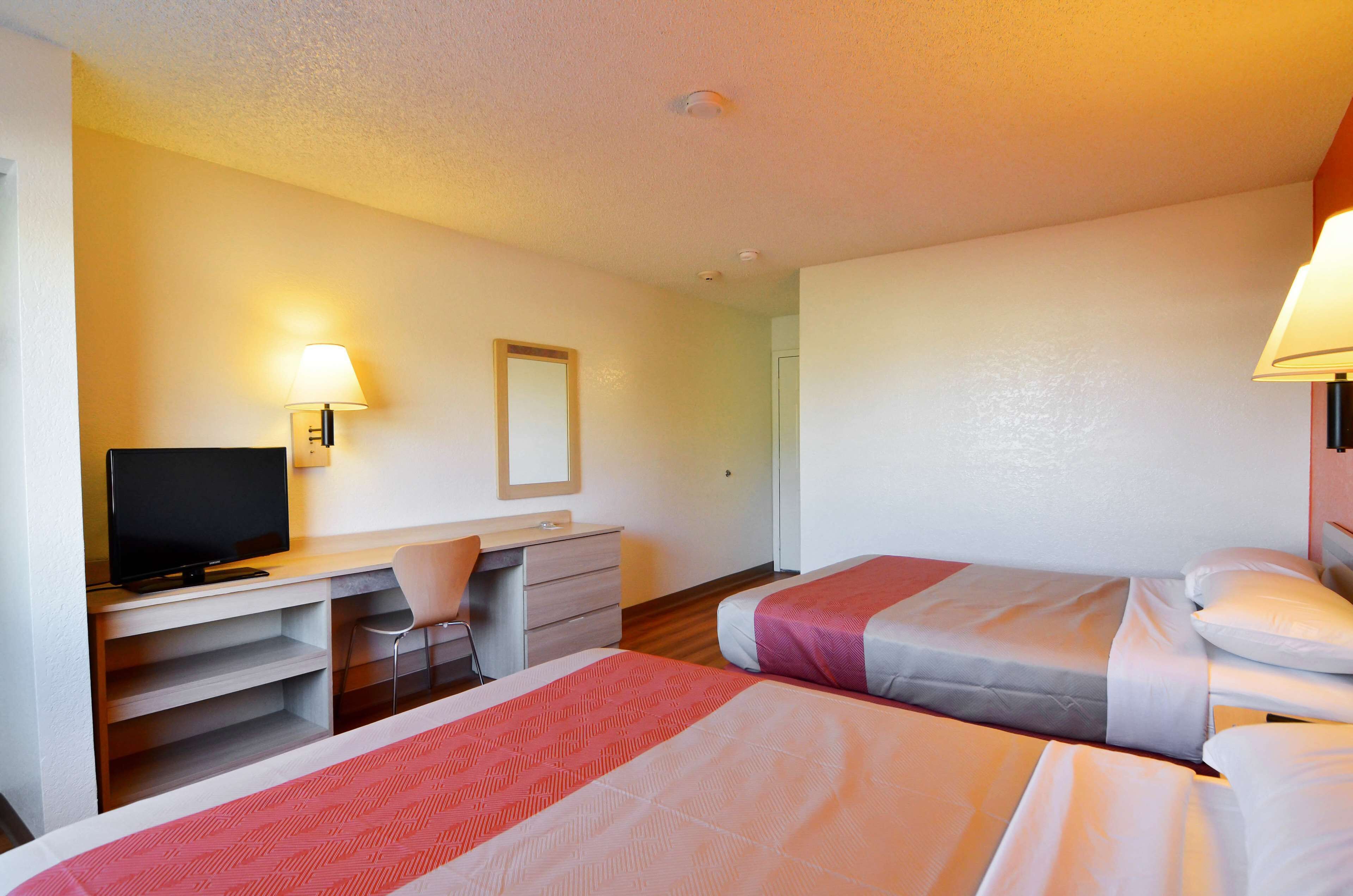 A hotel room with two beds, a desk with a chair, a television, and a lamp.