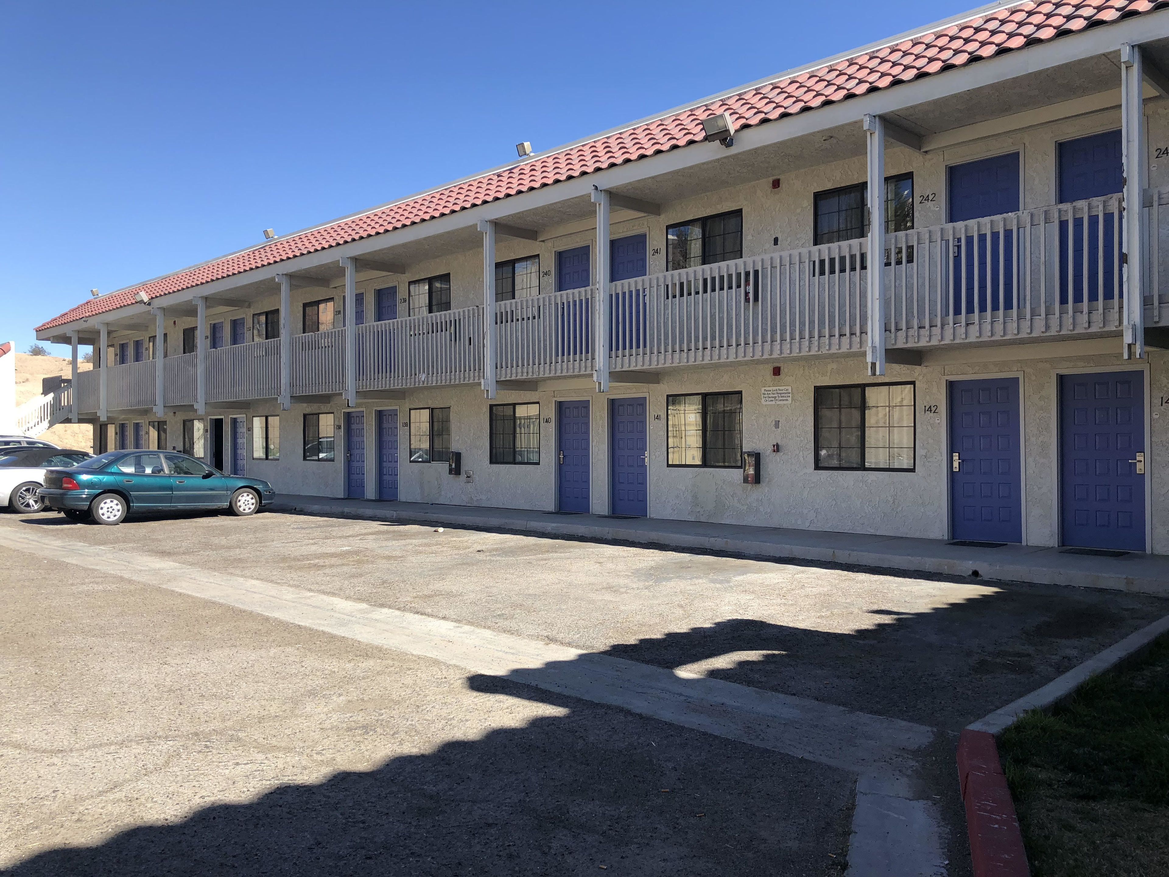 A multi-story motel with individual rooms, a parking area, and a blue car parked in front.