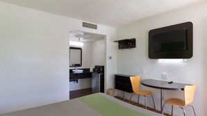 A hotel room with a bed, a desk, two chairs, a TV mounted on the wall, a small kitchenette, and a bathroom visible through an open door. - Motel 6 Barstow, CA (Barstow)