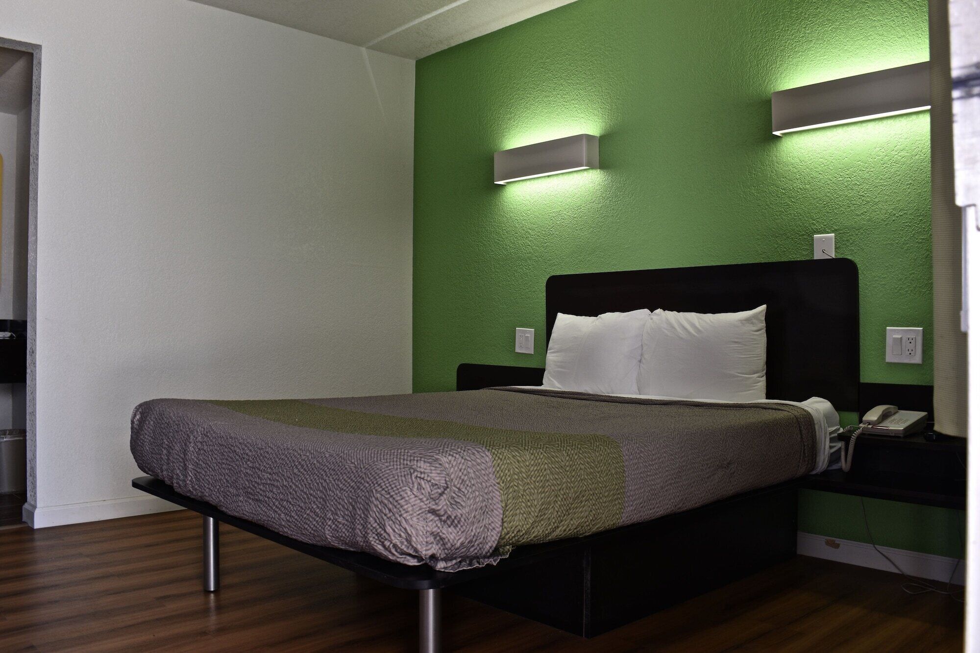 Een hotelkamer met een bed, nachtkastje, telefoon en twee wandlampen.