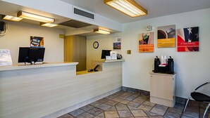 A reception area with a wooden reception desk, a clock, and a coffee station. - Motel 6 Barstow, CA (Barstow)