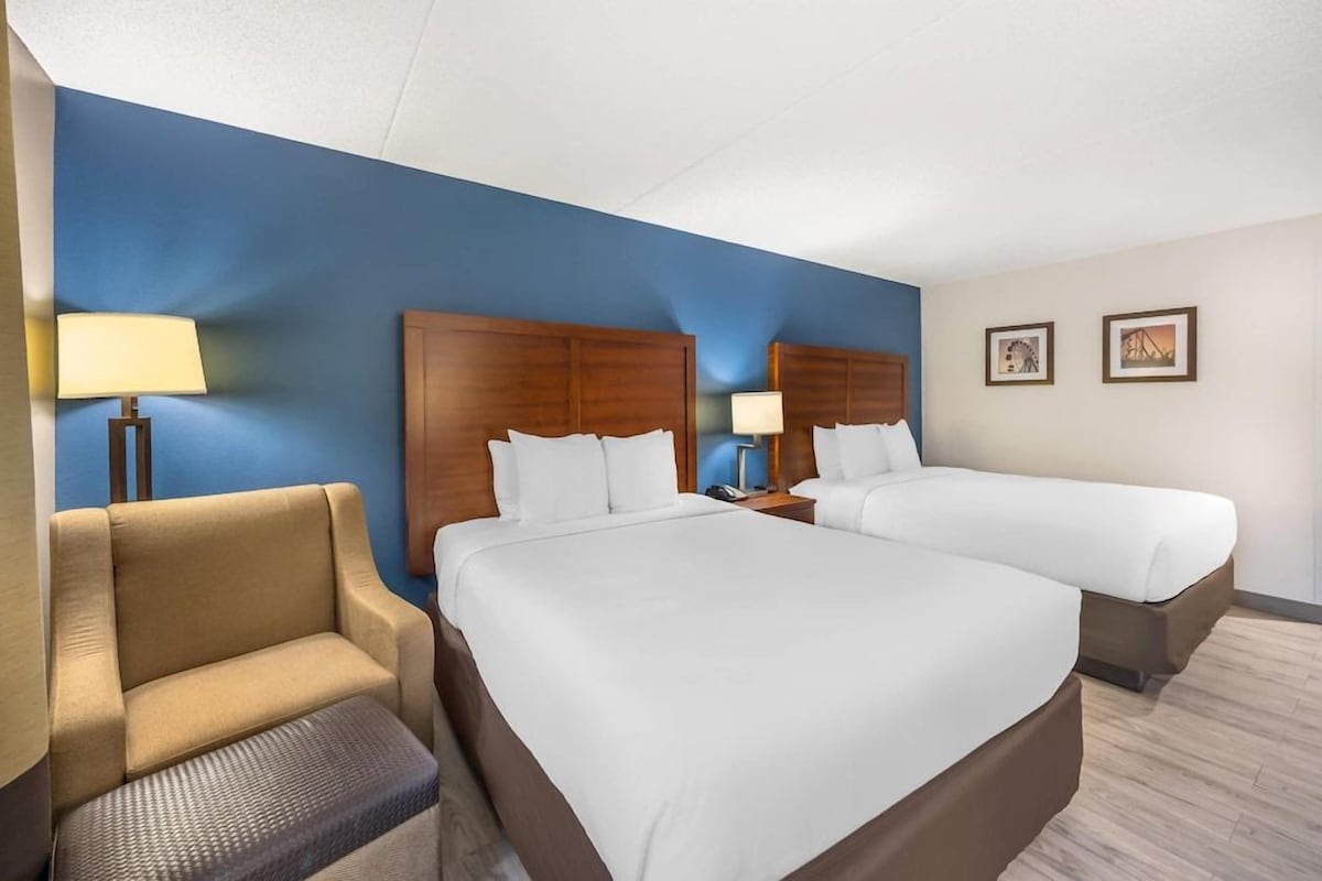 A hotel room with two beds, a chair, a lamp, and two framed pictures on the wall.