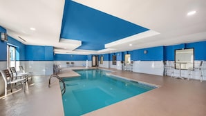 An indoor swimming pool with clear blue water, surrounded by lounge chairs and a seating area.