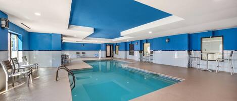 An indoor swimming pool with clear blue water, surrounded by lounge chairs and a seating area.