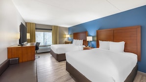 A hotel room with two beds, a desk, a TV, and a window with curtains.