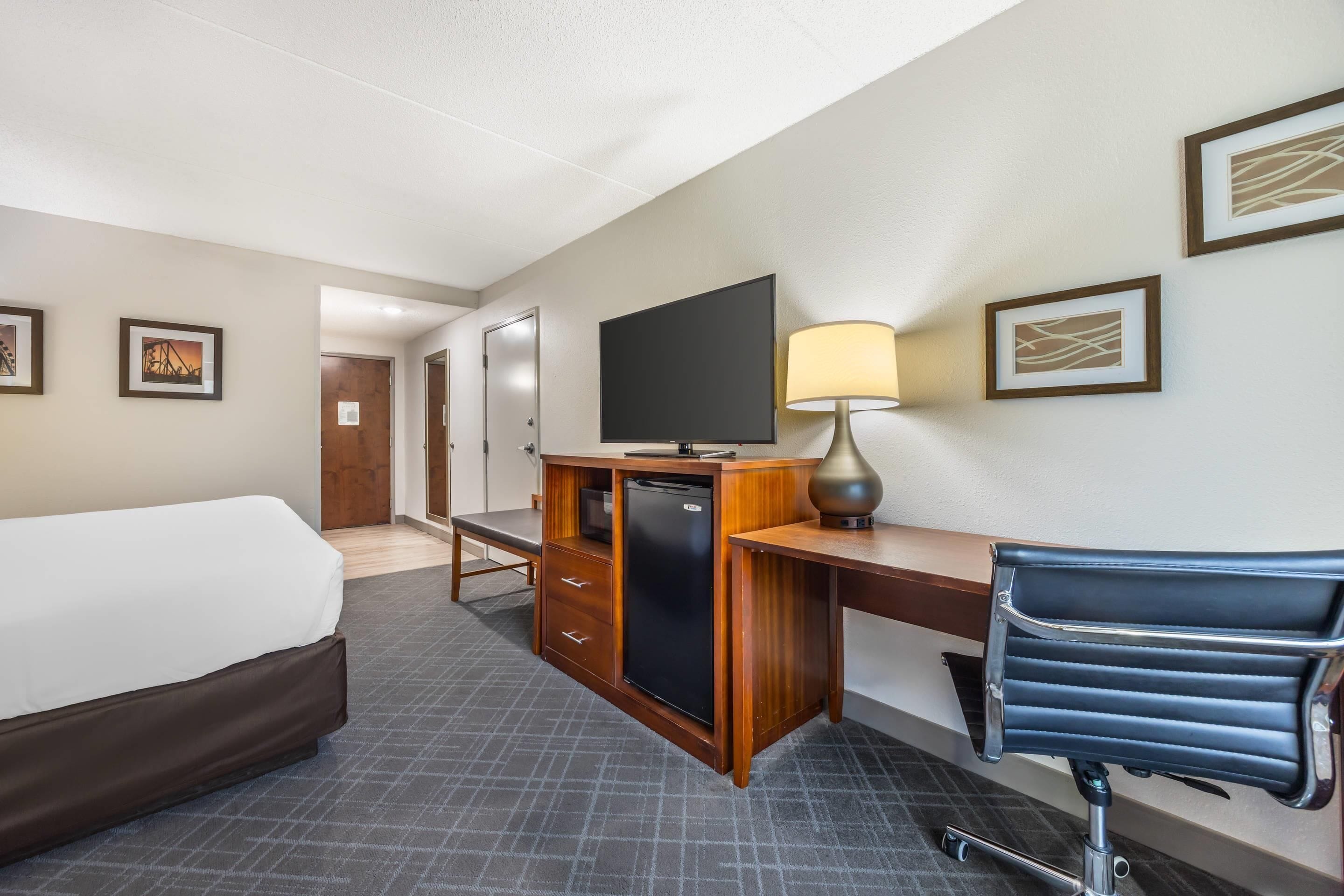 Une chambre d’hôtel avec un lit, un bureau équipé d’un ordinateur, une lampe, une télévision et une chaise.