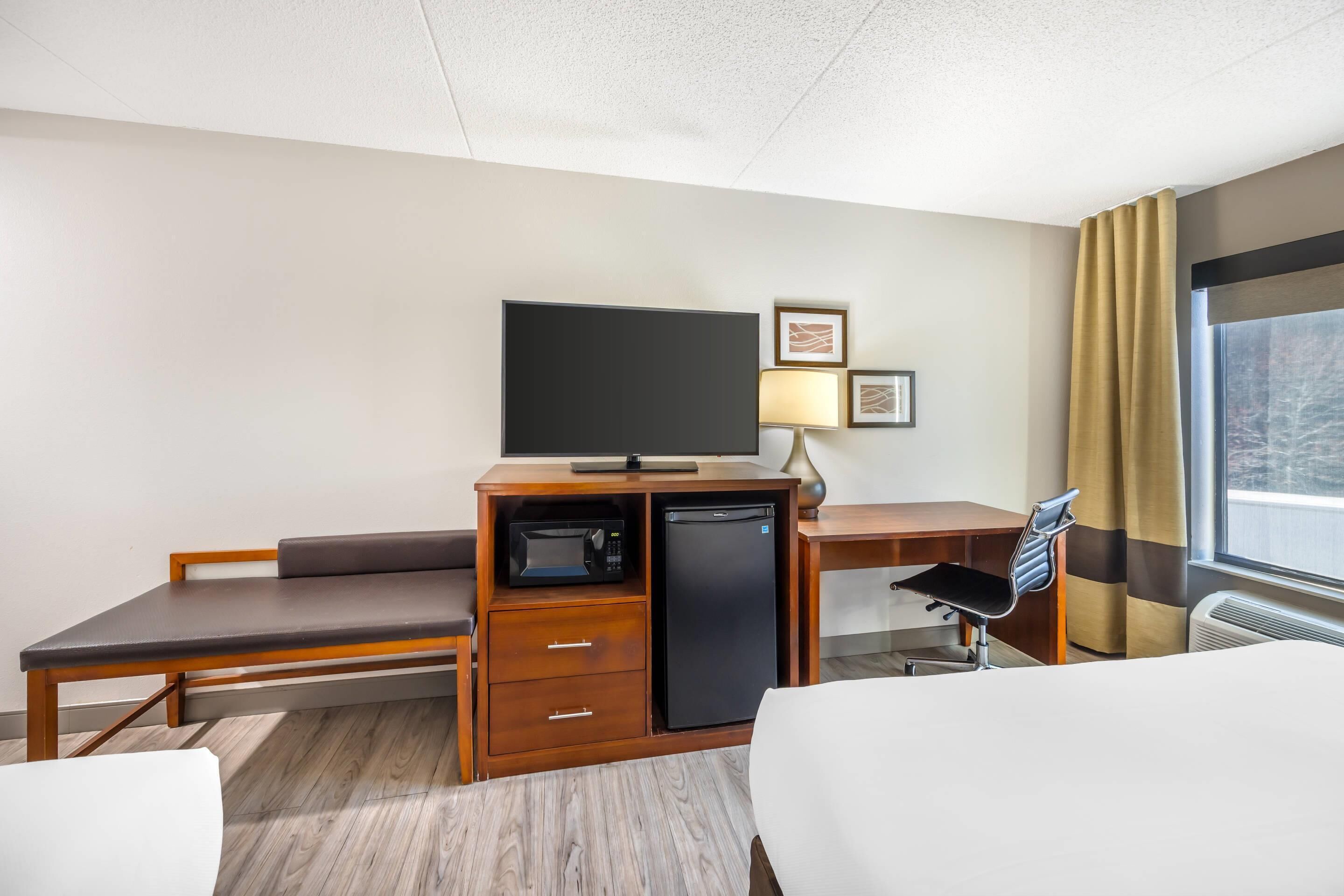 Une chambre d’hôtel équipée d’un lit, d’un bureau avec un ordinateur, d’un four à micro-ondes et d’une télévision.