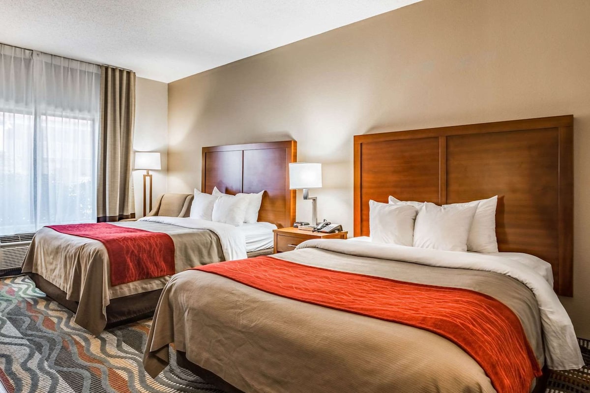 A hotel room with two beds, each with a red blanket, a wooden headboard, and a nightstand with a lamp.