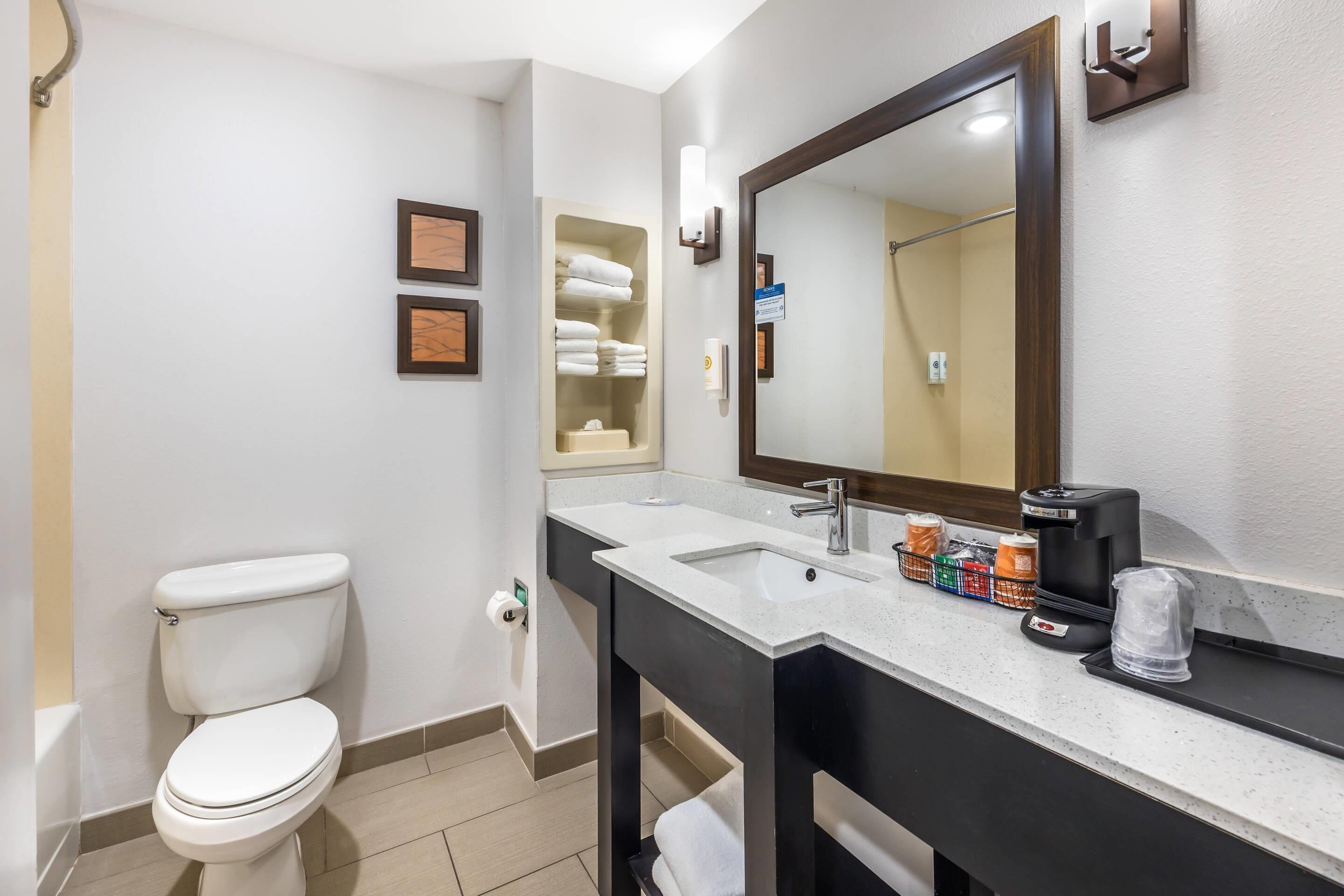 Un baño con inodoro, lavamanos, espejo y toallero.