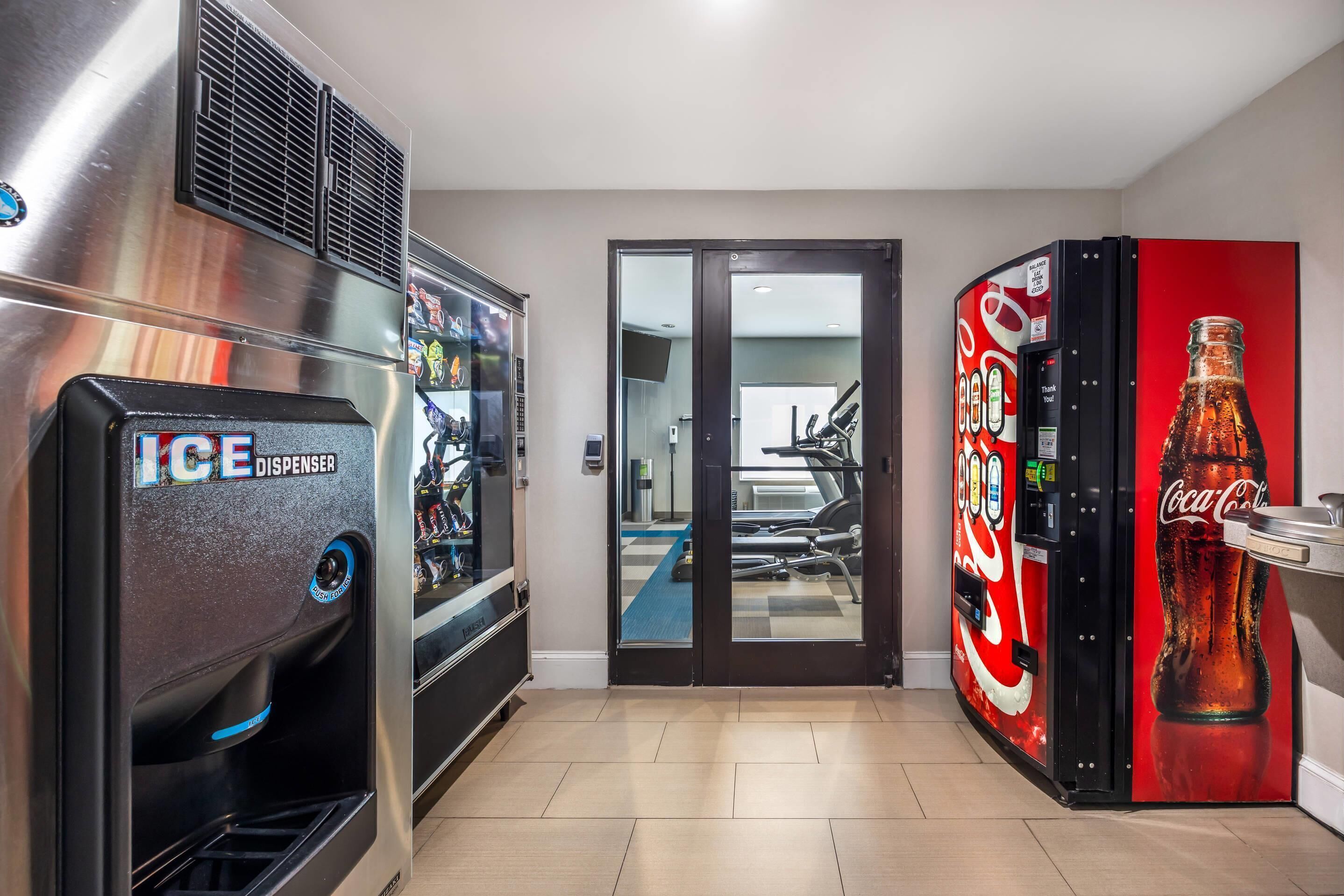 A hallway with a vending machine, a refrigerator, and a Coca-Cola dispenser.