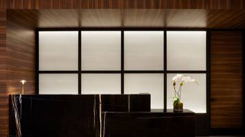 A reception area with a dark marble reception desk, a wooden panel wall, and a large window with frosted glass panels.