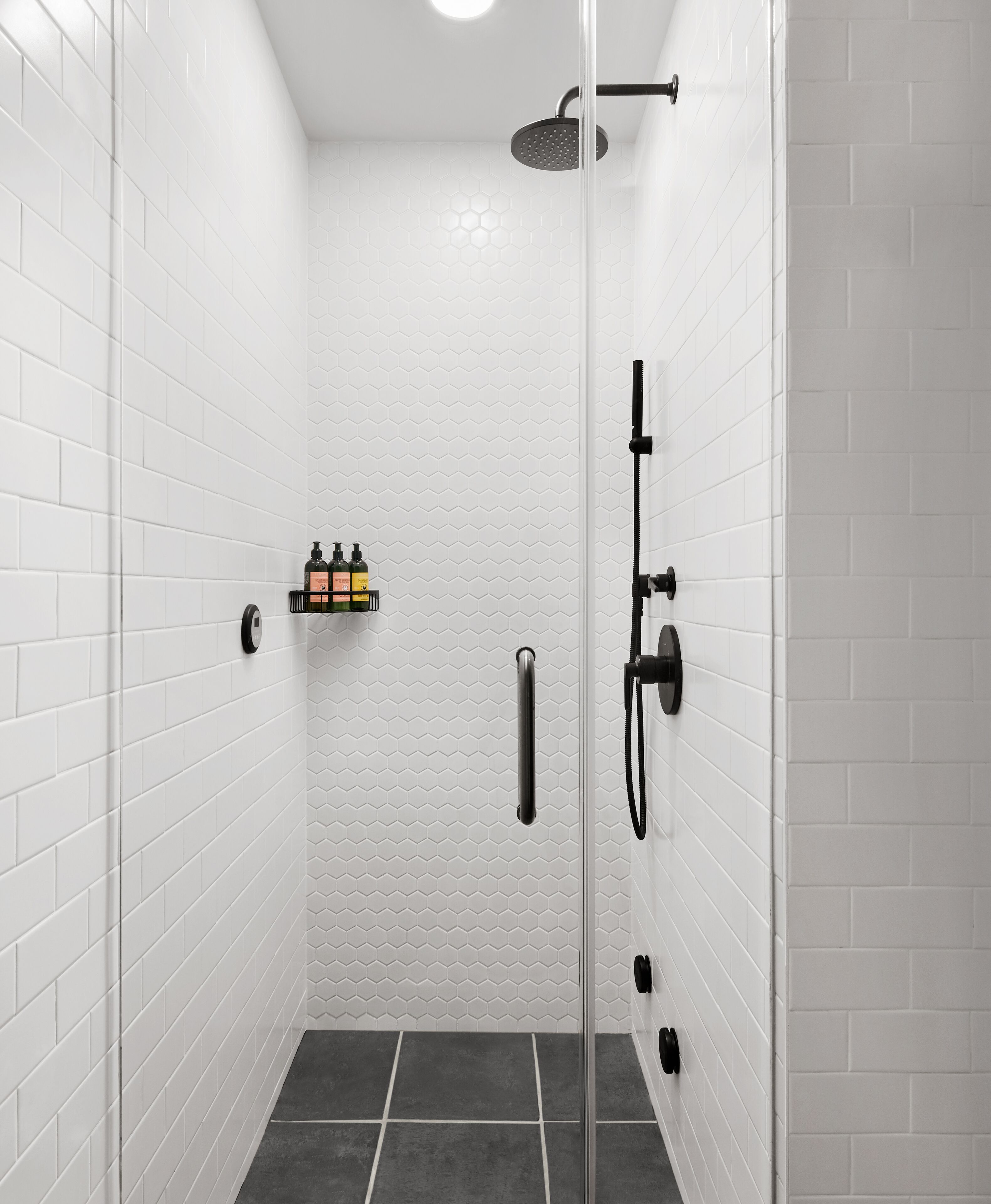 A modern shower with white tiled walls, a glass door, and a showerhead.