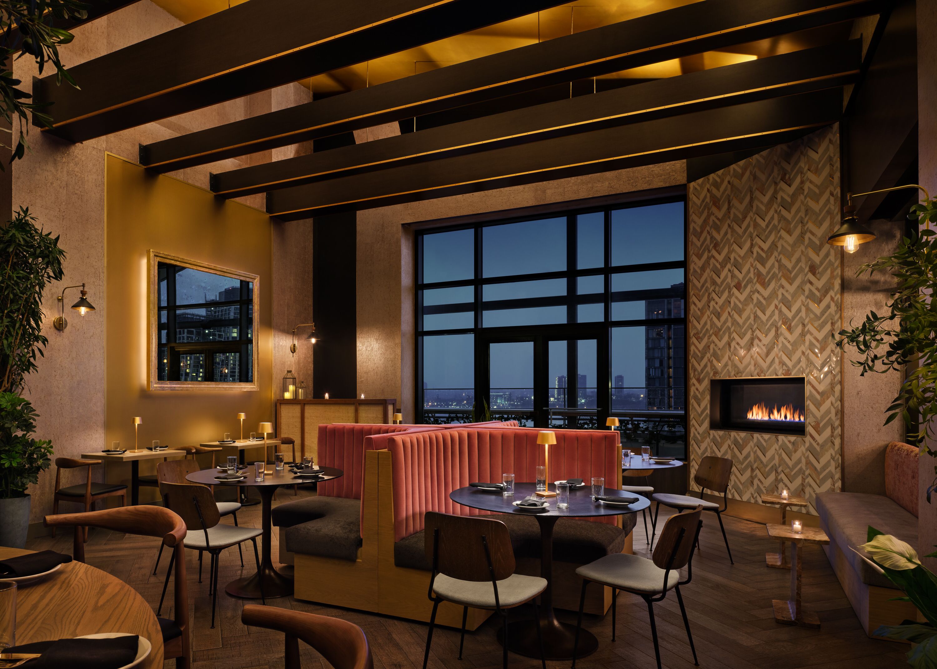 A modern restaurant with a high ceiling, large windows, and a fireplace. Tables and chairs are arranged for dining.