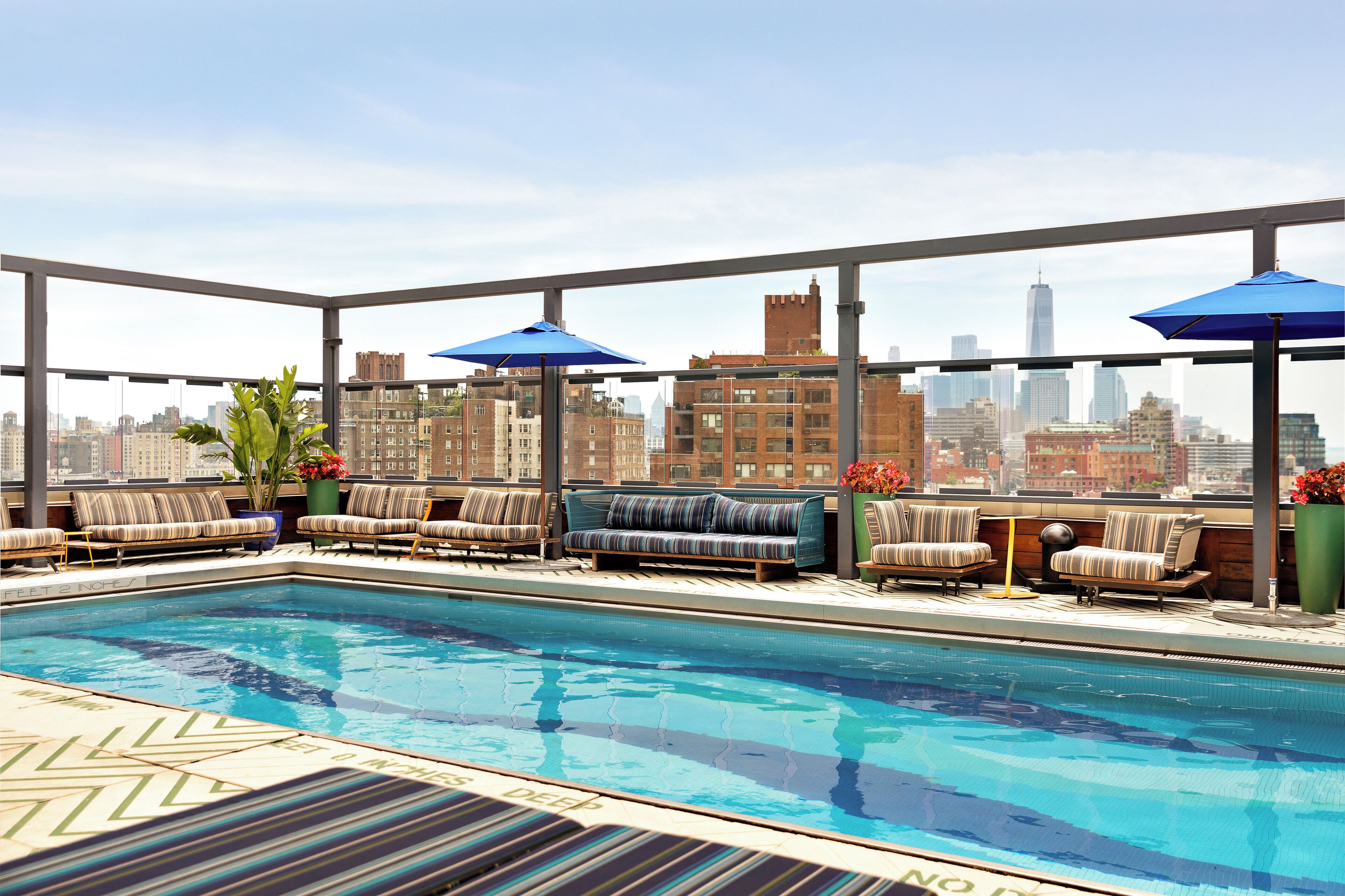 A rooftop pool area with seating and umbrellas, overlooking a city skyline.