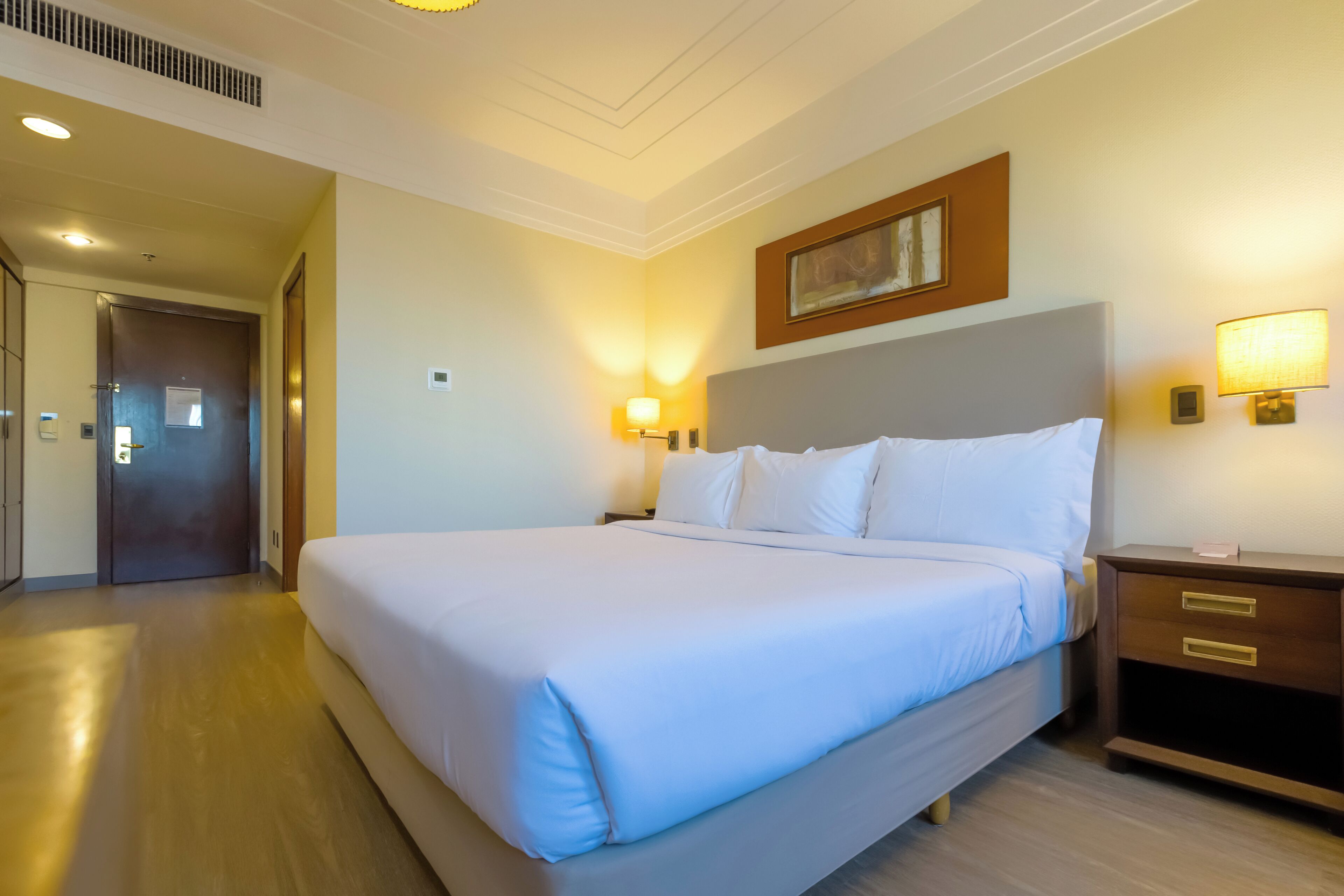 A hotel room with a large bed, bedside lamps, a nightstand, and a door.