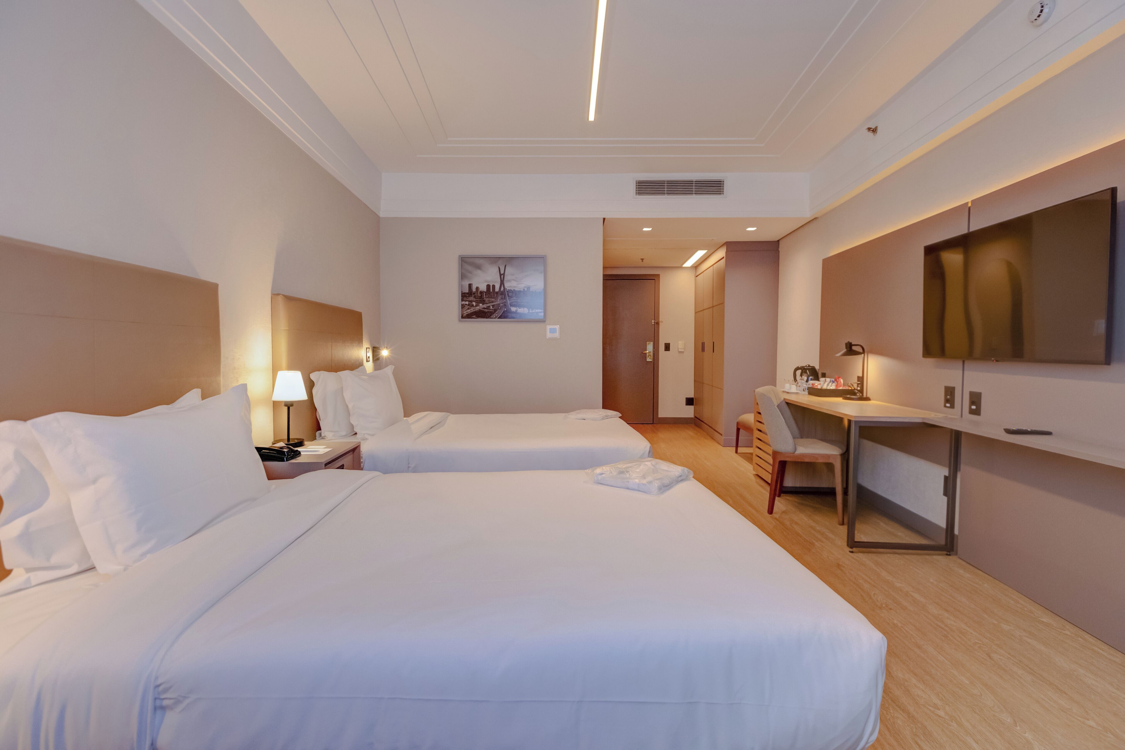 Habitación de hotel con dos camas, un escritorio, una silla, un televisor y un cuadro en la pared.