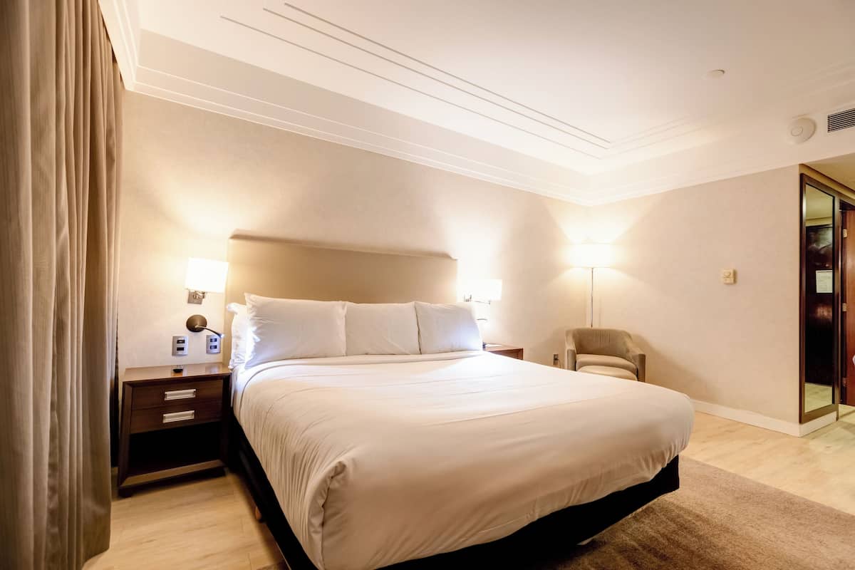 A hotel room with a large bed, bedside tables, a chair, and a lamp.