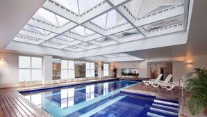 An indoor swimming pool with a skylight ceiling, wooden deck, and lounge chairs. - Radisson Hotel Alphaville (Barueri)