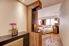 A hotel room with a bed, bedside table, mirror, potted plant, and scattered rose petals on the floor. - Radisson Hotel Alphaville (Barueri)