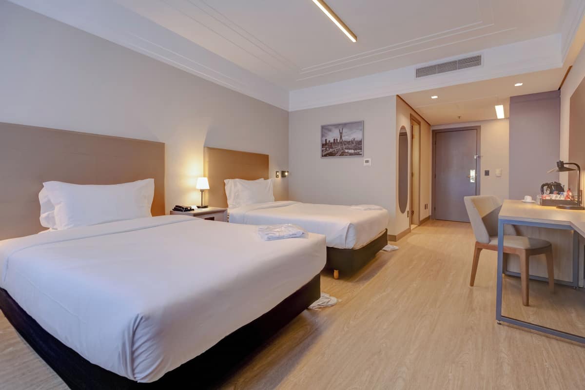 A hotel room with two beds, a desk, and a chair.