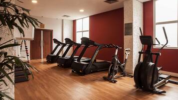 A gym with treadmills, an elliptical, and a stationary bike, wooden flooring, and a red wall.