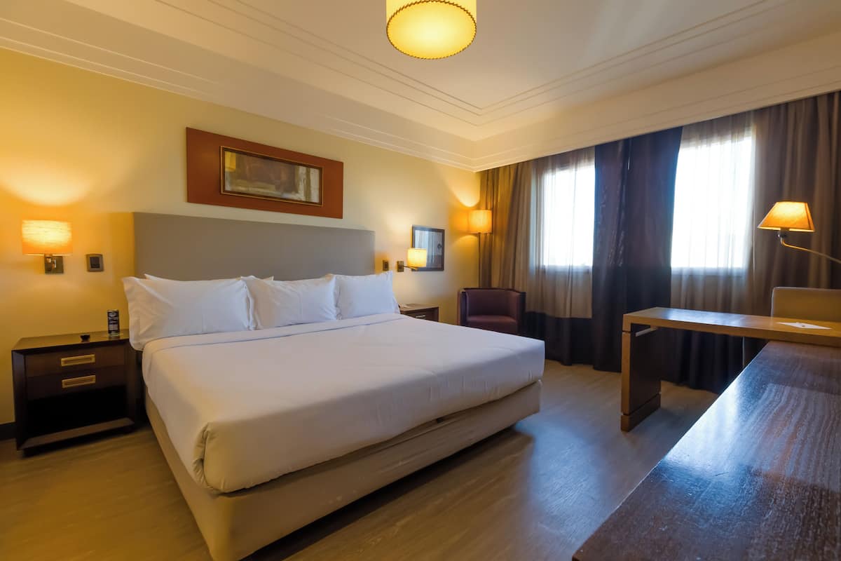 A hotel room with a large bed, bedside tables, a desk, and a chair.