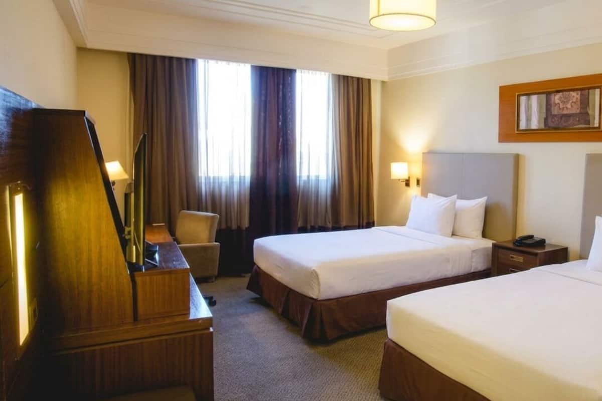 A hotel room with two beds, a desk, a chair, a television, and a window with curtains.