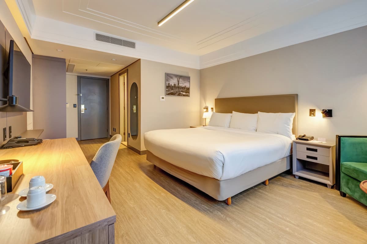 A hotel room with a large bed, a desk with a chair, a nightstand, and a green armchair.