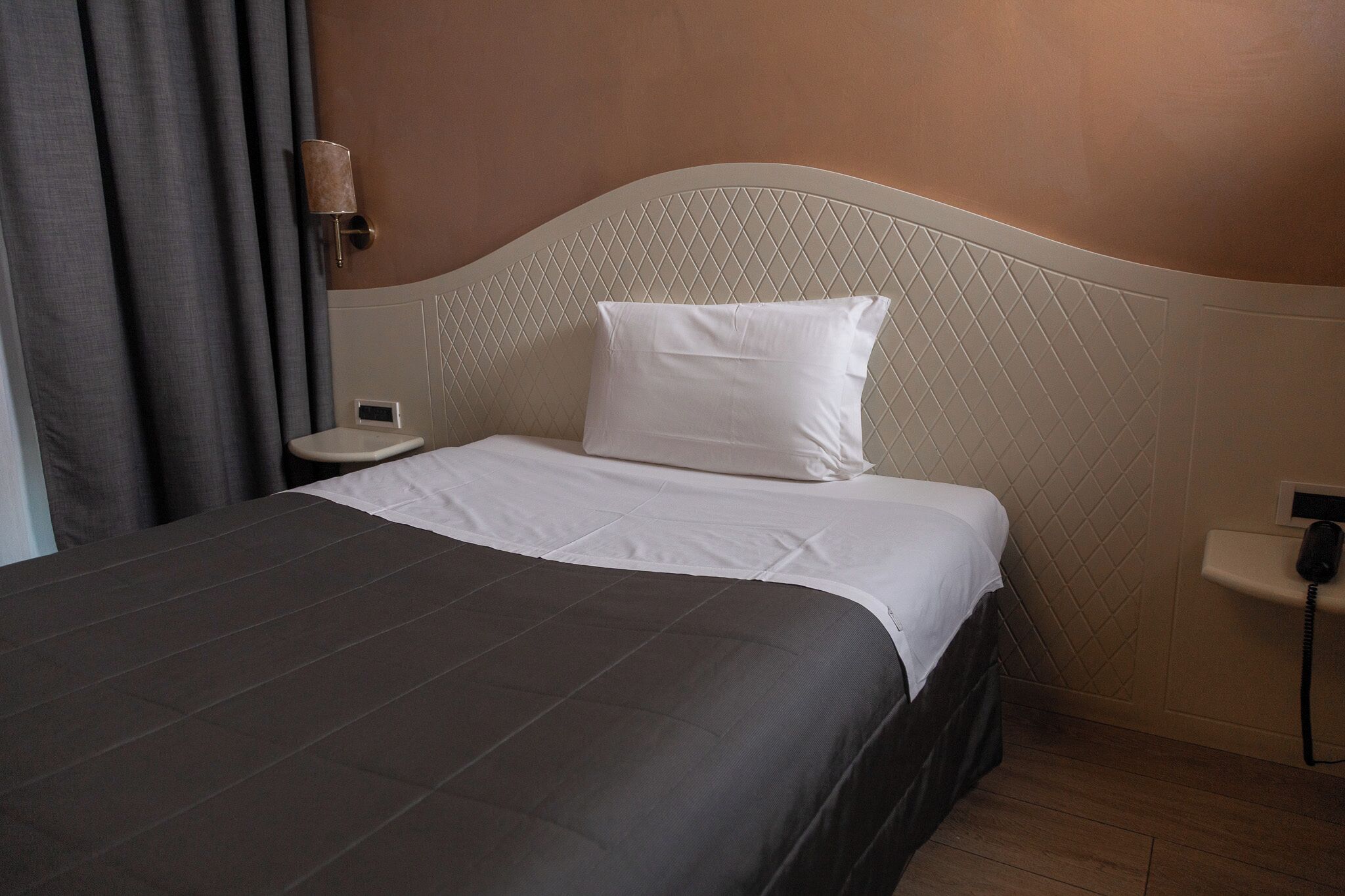 A hotel room with a bed, a bedside table, a lamp, and a telephone.