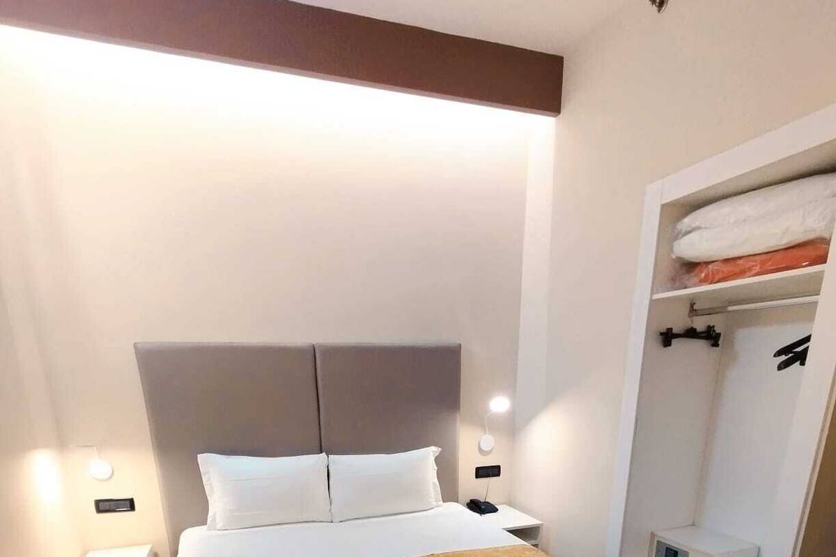 A hotel room with a bed, bedside tables, a wardrobe, and a shower area.