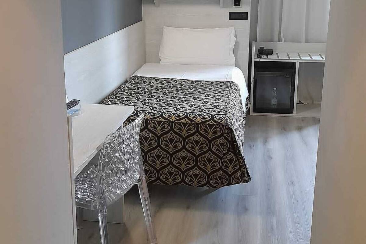 A hotel room with a bed, a desk, a chair, a small refrigerator, and a bathroom with a shower.