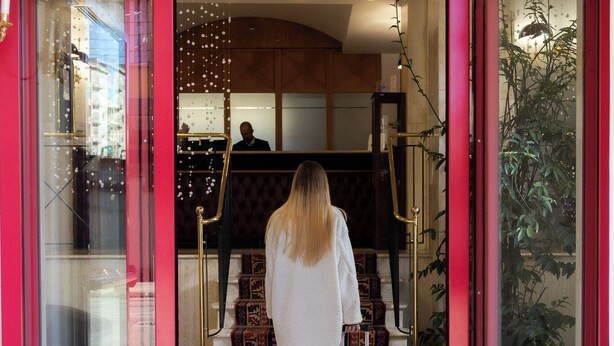 Entrada de un hotel con puerta roja, felpudo con el nombre del hotel y una escalera que conduce al interior.