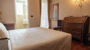 Een hotelkamer met een groot bed, een houten dressoir, een spiegel en een raam met gordijnen.