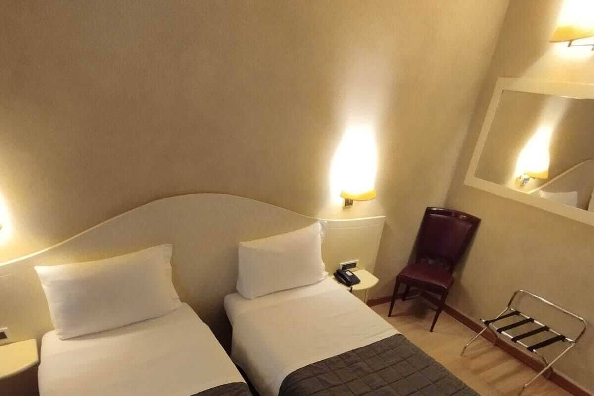 A hotel room with two single beds, a chair, a small table, and a mirror.