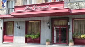 Un hotel con toldo rojo, amplias ventanas y plantas en macetas.