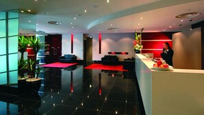 A modern hotel lobby with a reception desk, seating area, and potted plants.