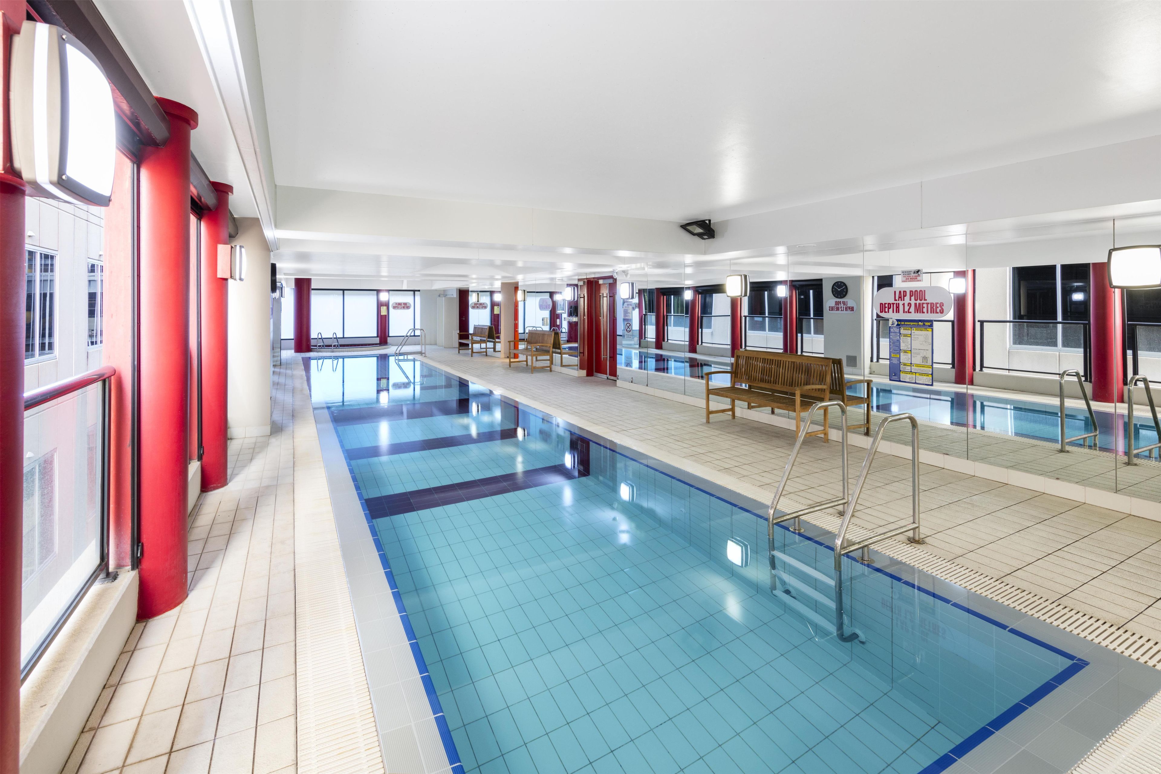 Una piscina con piso de baldosas, bancos y un cartel que indica la profundidad.
